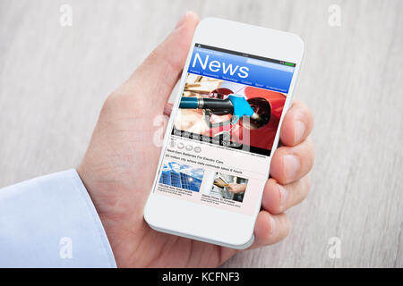 Close-up di persona le mani con il telefono cellulare che mostra le notizie sulla scrivania in legno Foto Stock