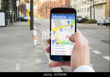 Close-up di persona della mano utilizzando la navigazione gps nel cellulare per trovare gli alberghi Foto Stock