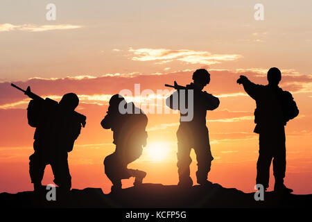 Silhouette di soldati armati con le armi contro il cielo climatiche sul campo di battaglia Foto Stock