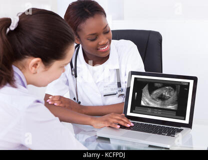 Felice medico donna che mostra la scansione a ultrasuoni del bambino sul laptop per il suo paziente presso la clinica Foto Stock