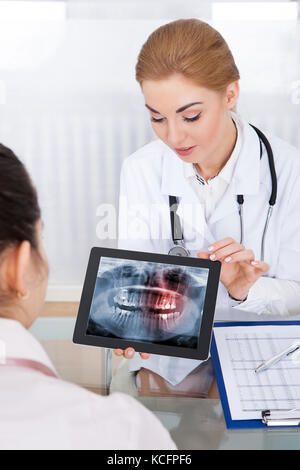Medico donna che mostra denti X-ray al suo paziente sulla tavoletta digitale Foto Stock