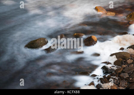 Una lunga esposizione prese con un arresto 10 filtro di acqua che scorre attorno ad un piccolo masso nel fiume swale, North Yorkshire, Inghilterra Foto Stock