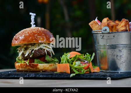 Cheeseburger con pomodoro, rucola, insalata coleslaw in una brioche bun e una benna di chunky chips, patatine fritte. Foto Stock