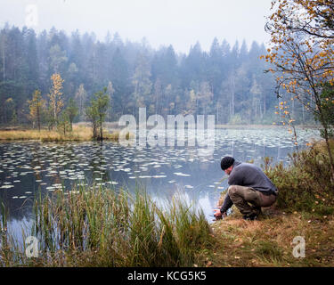 Escursionista lavando il suo volto alla mattina autunnale nel parco nazionale, Finlandia Foto Stock
