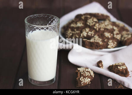 Biscotti al cioccolato con semi di sesamo in un piatto vintage e un bicchiere di latte su fondo in legno Foto Stock
