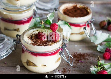 Dessert fatti in casa il tiramisù con lamponi in un vasetto di vetro sul vecchio sfondo di legno Foto Stock