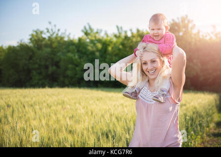 Madre bambino portando la figlia Piggyback e in piedi dal campo di grano Foto Stock