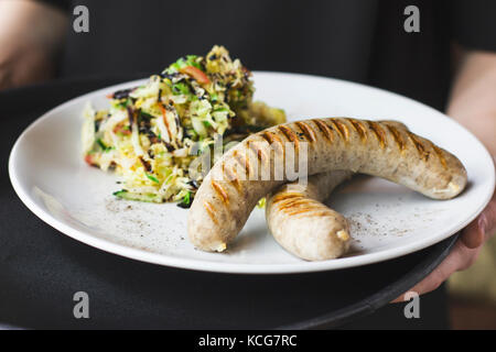 Il cameriere azienda salsicce bavarese con insalata di verdure fresche sul vassoio Foto Stock