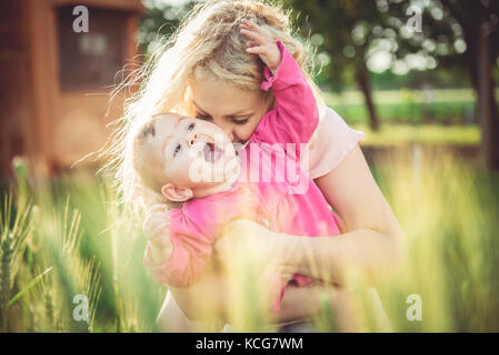 Giovane madre holding e baciare il suo bambino in erba Foto Stock