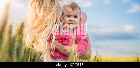 Felice madre tenendo la sua bambina le braccia nel campo di grano Foto Stock