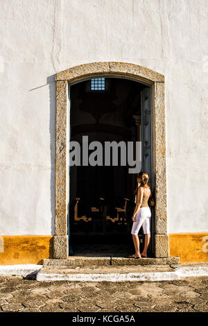 Giovane donna alla porta che guarda all'interno di una chiesa del distretto di Santo Antonio de Lisboa. Florianopolis, Santa Catarina, Brasile. Foto Stock