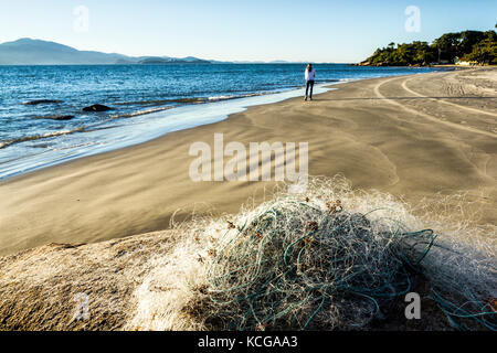 Rete da pesca su roccia e donna solitaria sullo sfondo di Forte Beach. Florianopolis, Santa Catarina, Brasile. Foto Stock