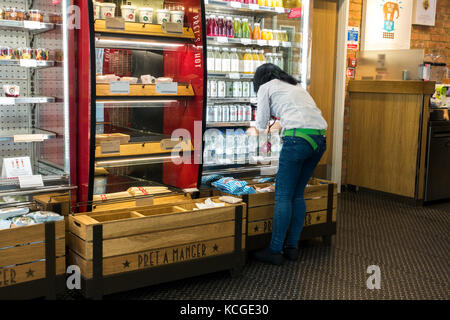 Un dipendente di sesso femminile il riempimento scaffali nelle bibite refrigerate visualizzatori in corrispondenza di un ramo di Pret a Manger in London, England, Regno Unito. Foto Stock