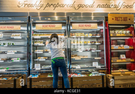 Un dipendente di sesso femminile il riempimento di ripiani con panini freschi in refrigerate visualizzatori in corrispondenza di un ramo di Pret a Manger in London, England, Regno Unito. Foto Stock