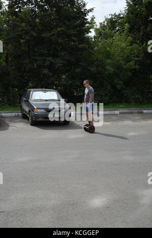 Uomo in casual abbigliamento sportivo cavalca un segway scooter in un parcheggio auto indossando occhiali da sole Foto Stock