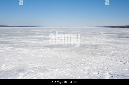 Bay ricoperto di ghiaccio con impronte e tracce, sotto il cielo blu chiaro, contro shore su entrambi i lati, sul lago simcoe, ontario, Canada. Foto Stock