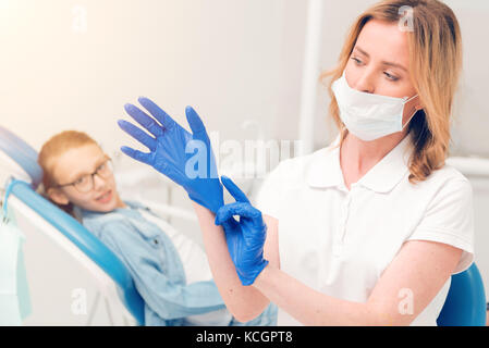 Focalizzato il dentista a mettere su guanti medicali Foto Stock