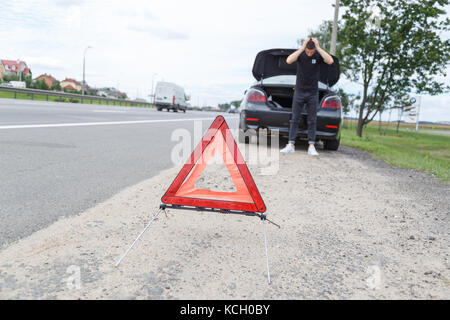 Una vettura con una disaggregazione a fianco della strada, uomo imposta il triangolo di avvertenza Foto Stock