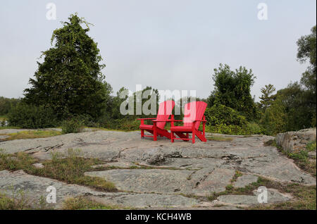 Due red adirondack sedie su una collina di granito in un parco Foto Stock