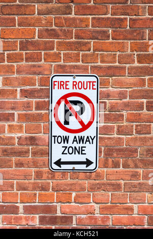 Un segno rosso di un muro di mattoni avverte di non parcheggio,fire rotta e trainare la zona al di fuori di un edificio. Foto Stock