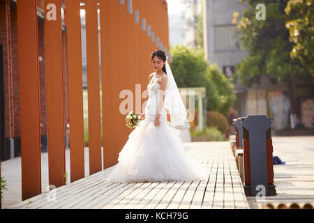 Outdoor Ritratto di giovane e bella asiatica sposa con bouquet in mano. Foto Stock