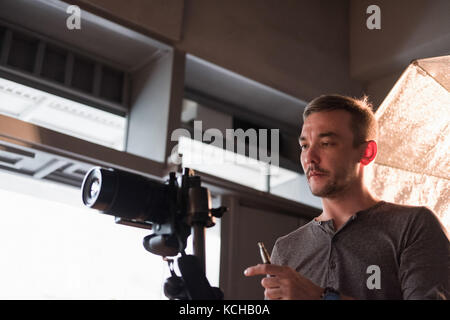 Un giovane fotografo imposta la fotocamera in studio su uno sfondo di illuminazione Foto Stock