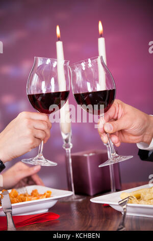 Primo piano della mano della coppia che tiene il vino rosso e tostando il vetro Foto Stock