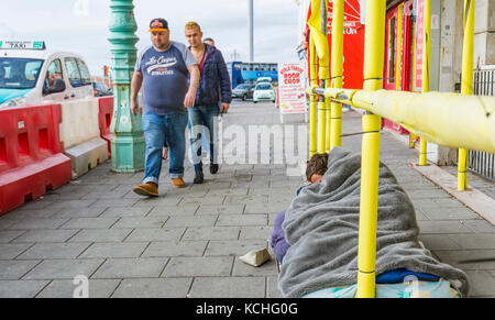 L'uomo sonno agitato per le strade di Brighton in East Sussex, England, Regno Unito, con la gente che camminava passato ignorando lui. Foto Stock