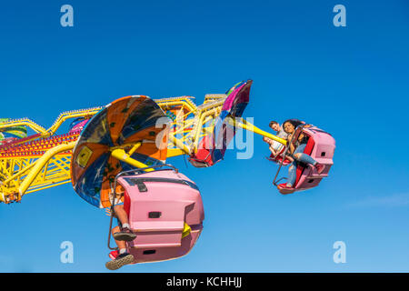I giovani godono di un estate fairground ride su ombrelli sotto il cielo blu Foto Stock