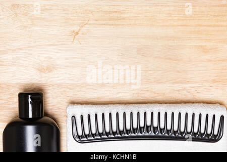 La cura dei capelli e styling. Sfondo nero bottiglia, ampia pettine a denti bianchi e Terry asciugamano panno sulla superficie di legno. spazio copia Foto Stock