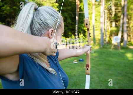 Certi giovani femmine archer di puntamento a freccia sulla scheda target nella foresta Foto Stock