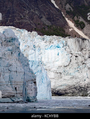 I toni del blu attraverso il ghiaccio del ghiacciaio margerie sono molto colorati e splendidamente di contrasto contro la montagna rocciosa dietro di essa Foto Stock