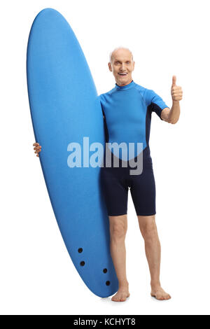 A piena lunghezza Ritratto di un senior in un tipo di muta in possesso di una tavola da surf e per la fabbricazione di un pollice in alto gesto isolato su sfondo bianco Foto Stock