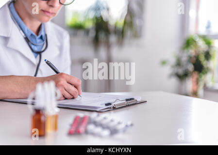 Forniture mediche sulla tavola e dottore in background la prescrizione di scrittura Foto Stock