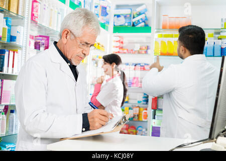 Il farmacista iscritto sulla clipboard mentre i colleghi che lavorano in farmacia Foto Stock