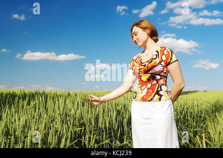 Ragazza sognante indossa camicetta fiorito e mantello bianco in piedi di frumento cornfield toccando delicatamente le pannocchie con le sue palme Foto Stock