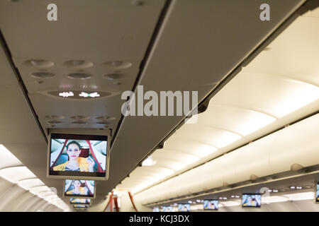 Monaco di Baviera, Germania, Settembre 21th, 2017: in volo di monitor collegati sul soffitto mostra un assistente di volo dando istruzioni di sicurezza, Aegean airlines. Foto Stock