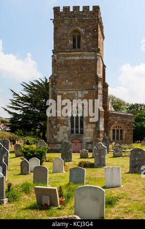 Il crenallated medievale torre della chiesa di St Nicholas metà nasconde un antico albero di Yew come ovelooks sagrato bagnata dalla metà giornata sole estivo Foto Stock