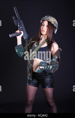 Bella giovane donna in uniforme militare con un mitragliatore su sfondo nero Foto Stock