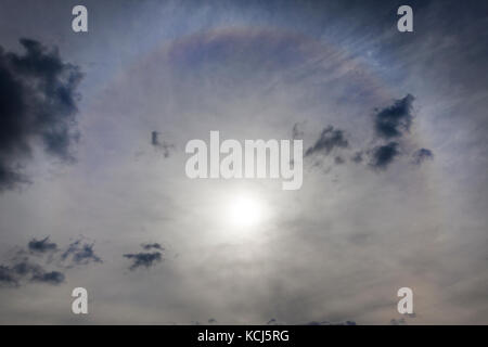 Un bellissimo alone solare in tempo nuvoloso. fotografia di close-up di sole e un cerchio colorato attorno alla stella, vista dal basso. Foto Stock