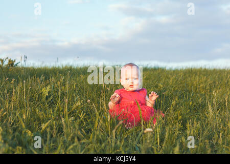 Carino Baby girl nel bel vestito siede in erba verde Foto Stock