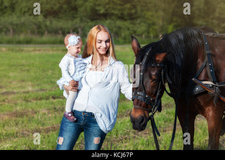 Mama e la sua piccola figlia in piedi in un prato in prossimità di un cavallo Foto Stock