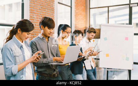 Multietnica variegato gruppo di felice giovane adulto utilizzando informazioni tecnologia gadget dispositivi insieme. team creativo, il lavoro di squadra, casual concetto aziendale Foto Stock