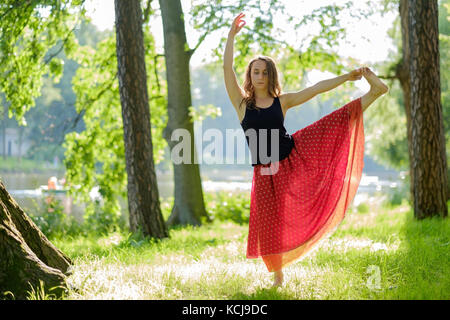 La donna caucasica nel mantello rosso equilibrio facendo yoga asana in estate park. Foto Stock