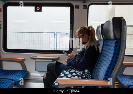 Malinconici donna che guarda il suo smartphone in un treno Foto Stock