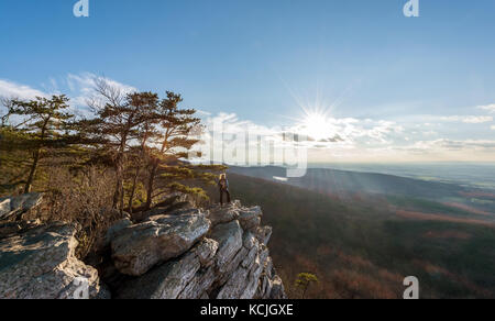 Escursionista femmina in piedi nel vento in corrispondenza di un bordo di una scogliera rocciosa sulla cima di una montagna appalachian godendo del tramonto e vista Foto Stock