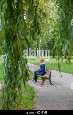 Donna bionda seduta sul banco sotto un albero, Lussemburgo Foto Stock