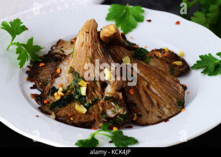 Frittura di funghi Oyster con aglio e prezzemolo con glassa di aceto balsamico in una piastra bianca su un nero sfondo astratto. un sano concetto. Foto Stock