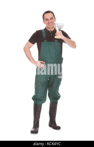 Felice lavoratore maschile tenendo una pala su sfondo bianco Foto Stock