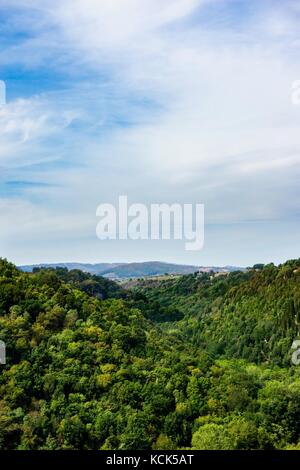 Foto verticale con vista nella piccola valle tra due colline o rocce ricoperte dal verde della foresta in Italia Toscana. il cielo è parzialmente blu ma principali Foto Stock